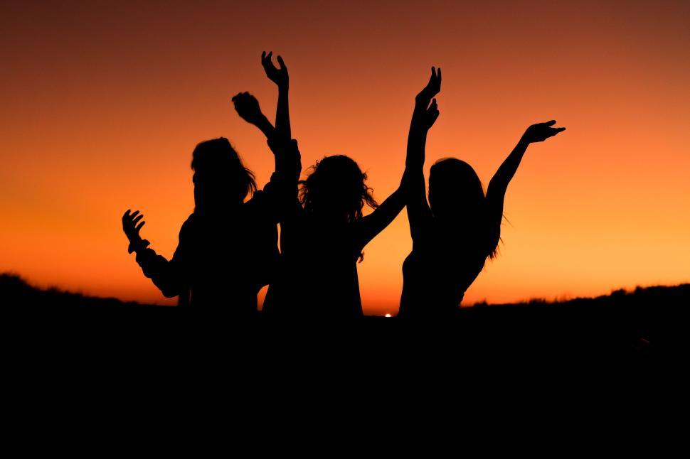 Free Image of Silhouettes of three people dancing joyfully at sunset time. 