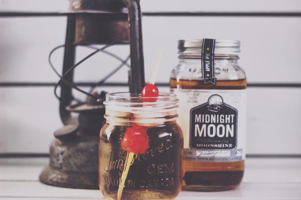 Free Image of Cocktail in mason jar with cherries beside bottle of moonshine 