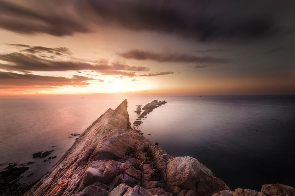 Free Image of Sunset over rocky coastline with dramatic clouds and calm ocean 