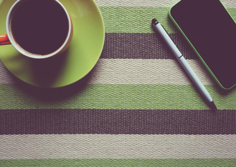 Free Image of Morning coffee with smartphone and pen placed on a green striped mat 