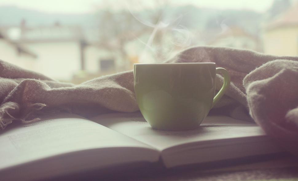 Free Image of Steaming cup of coffee sits on open book with cozy backdrop. 