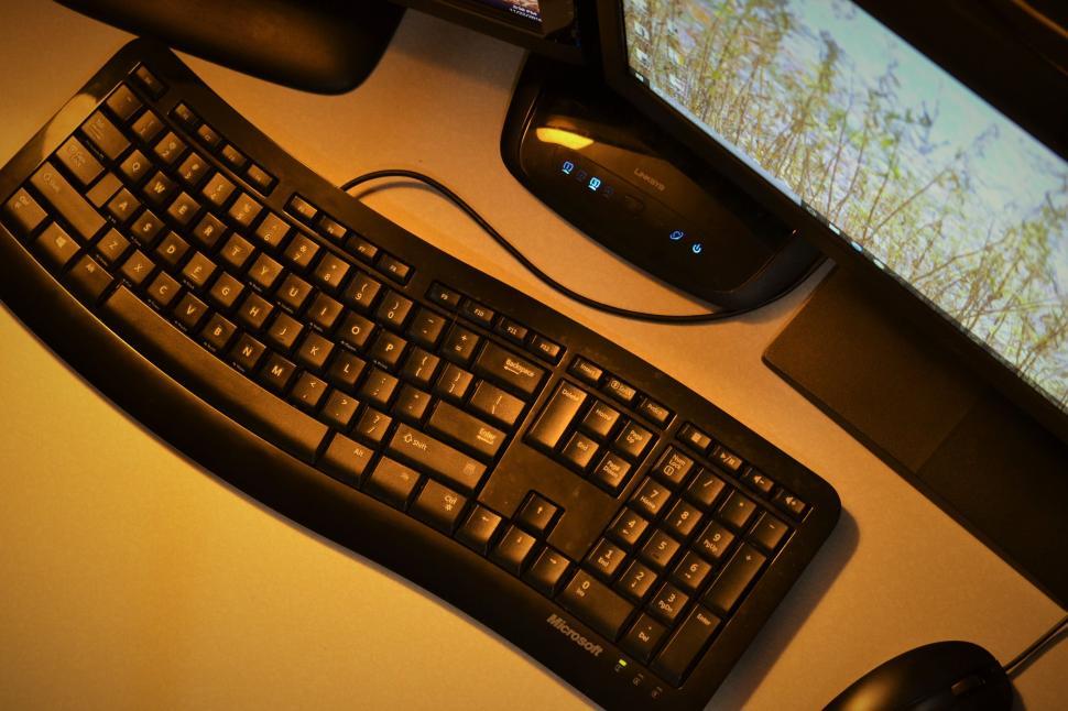 Free Image of Curved ergonomic computer keyboard on a desk next to a monitor. 