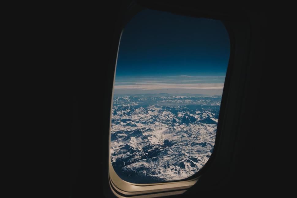 Free Image of Stunning aerial view of snow-capped mountains through airplane window 