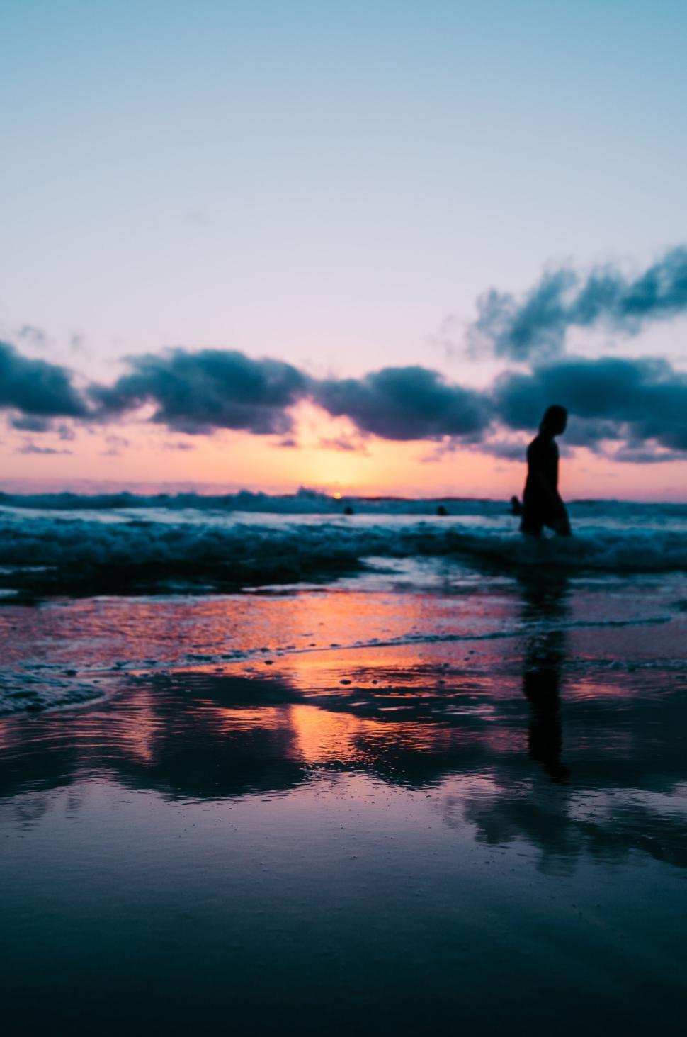 Free Image of Person walking along the beach at sunset with a colorful sky. 