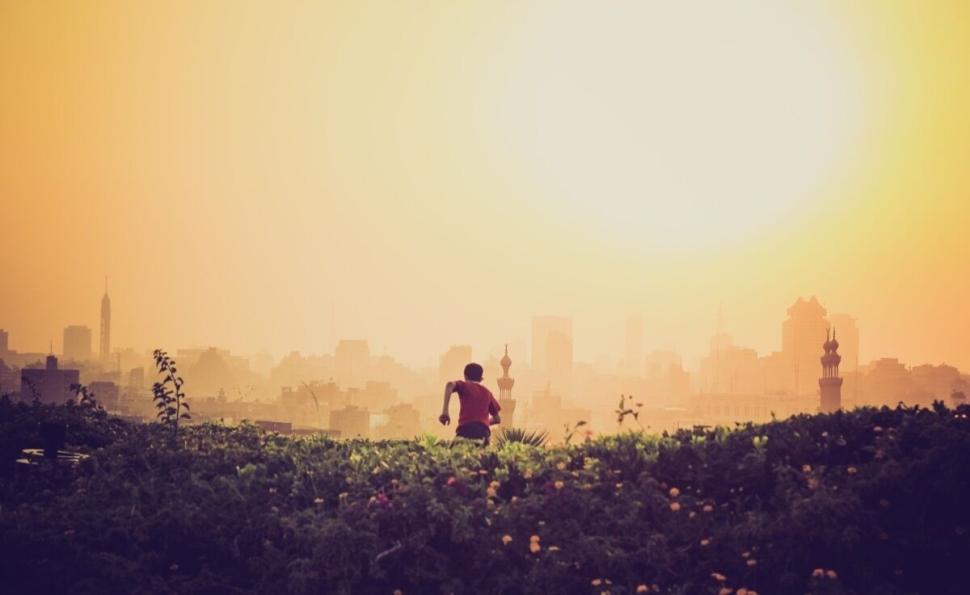 Free Image of Silhouette of a person running at sunrise with city skyline background. 