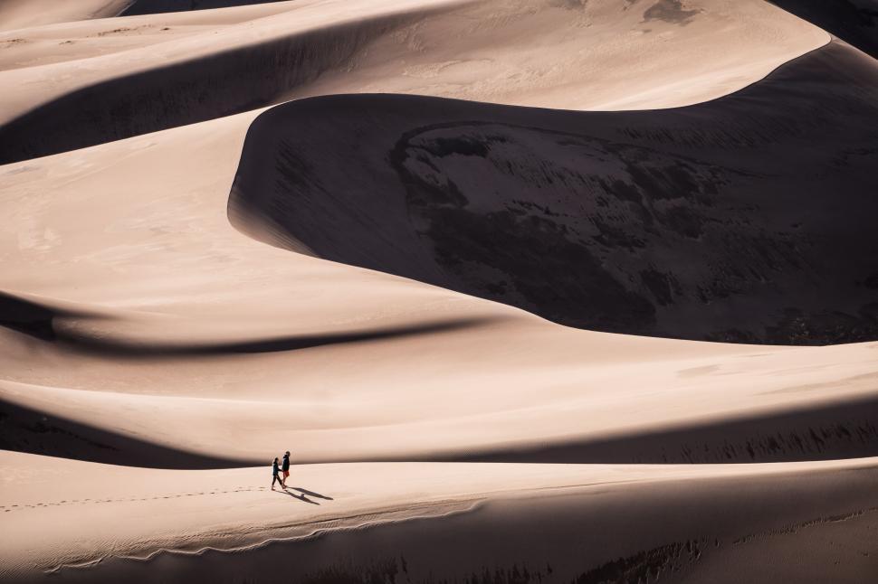 Free Image of Solitary person walking on vast sand dunes with long shadows 