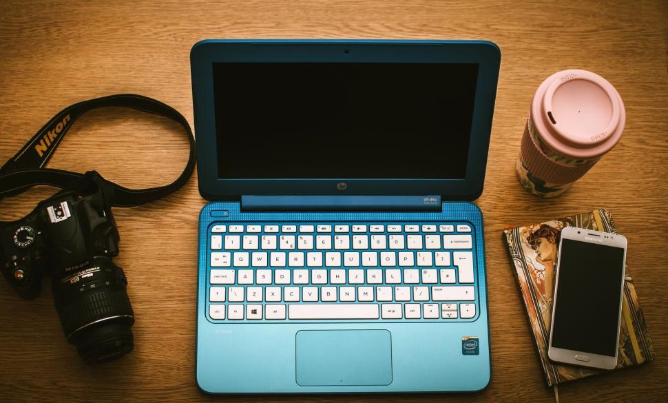 Free Image of Blue laptop and Nikon camera amidst tech accessories on wooden table. 