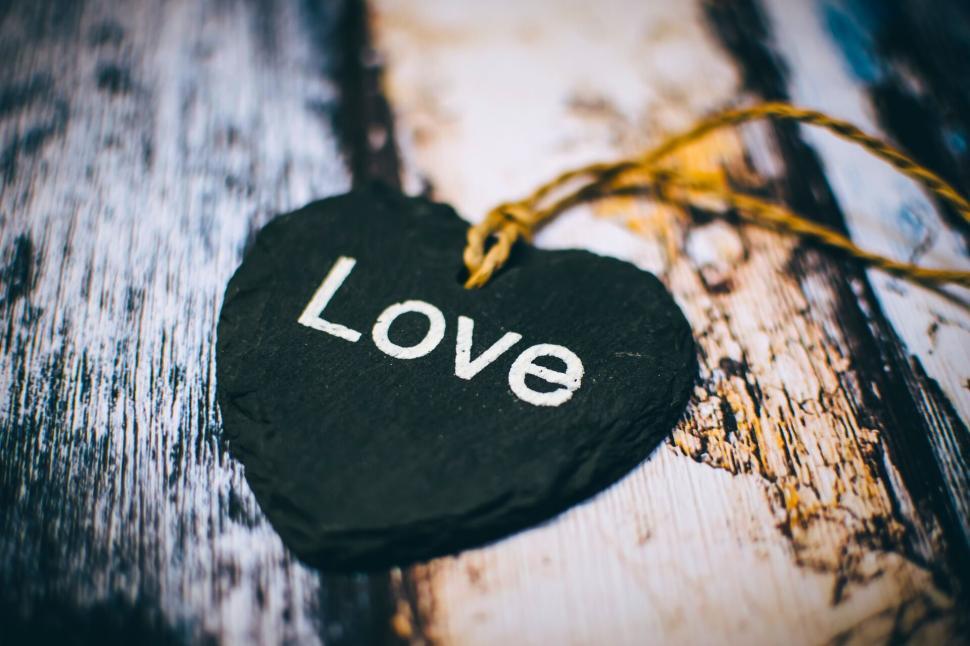 Free Image of Black slate heart with  Love  text hanging on rustic wooden wall 
