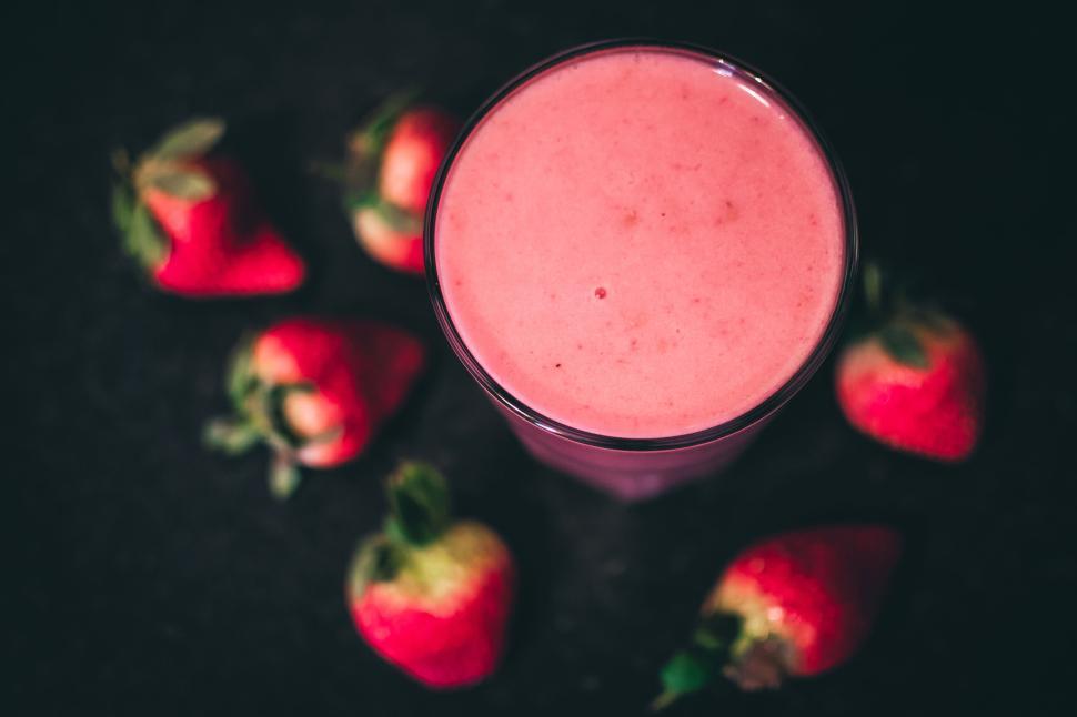 Free Image of Glass of strawberry smoothie with strawberries scattered around it 