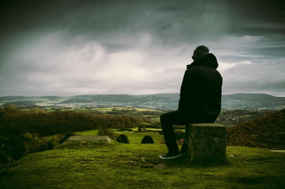 Free Image of Person sitting on a stone platform overlooking scenic landscape. 
