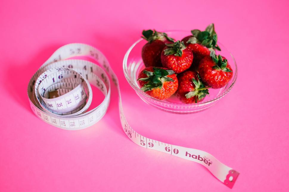 Free Image of Fresh strawberries in a bowl with measuring tape on pink background. 