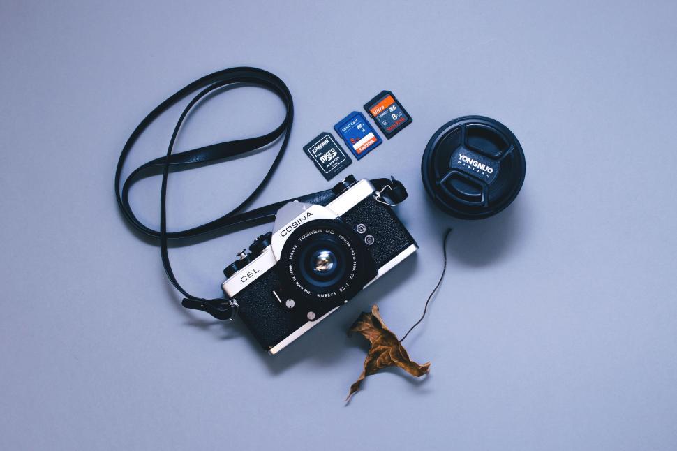 Free Image of Vintage camera with lens cap and memory cards on a flat surface. 