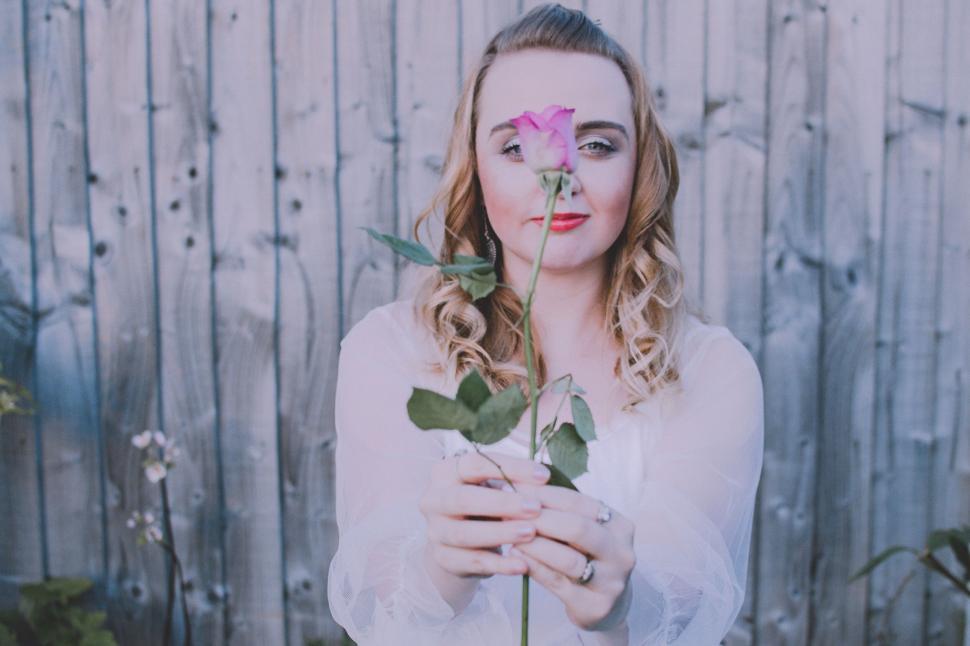 Free Image of Woman holding a rose in front of her face beside wooden fence 