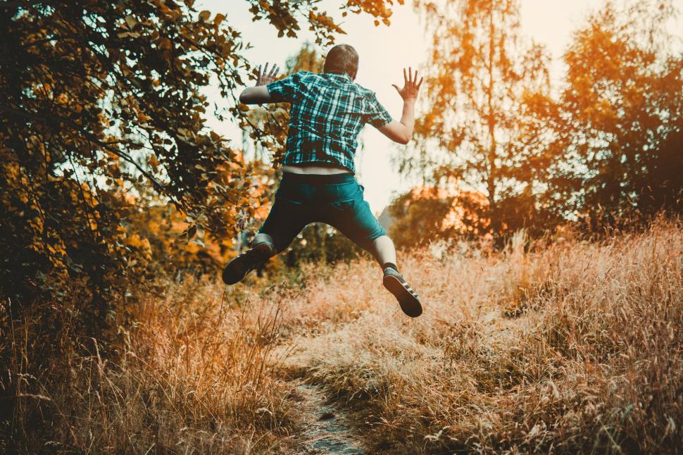 Free Image of Man jumping in nature wearing a plaid shirt during sunset time 