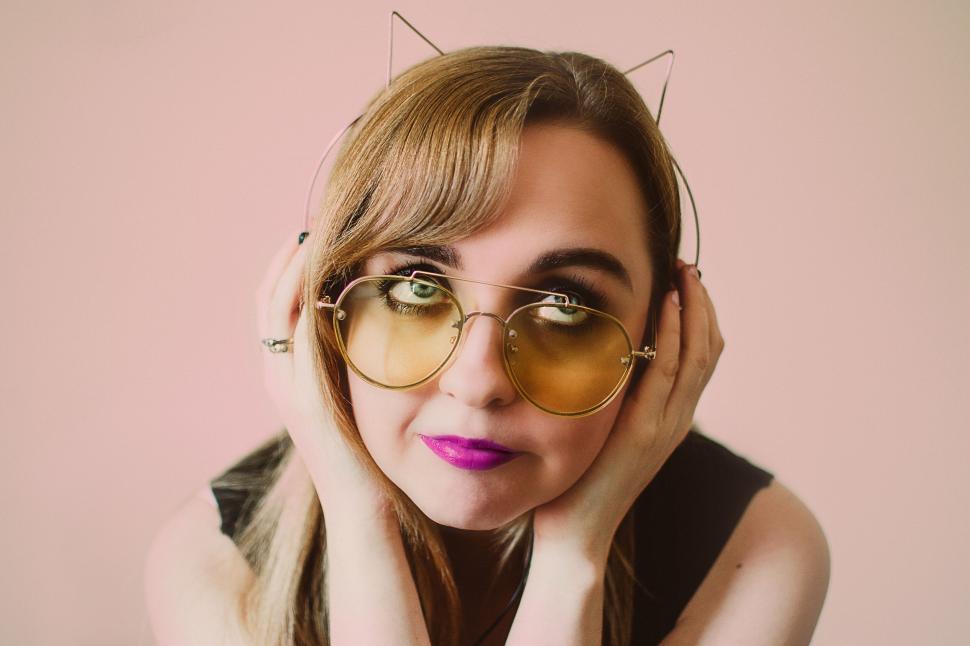 Free Image of Woman in sunglasses and cat ear headband with vibrant background 