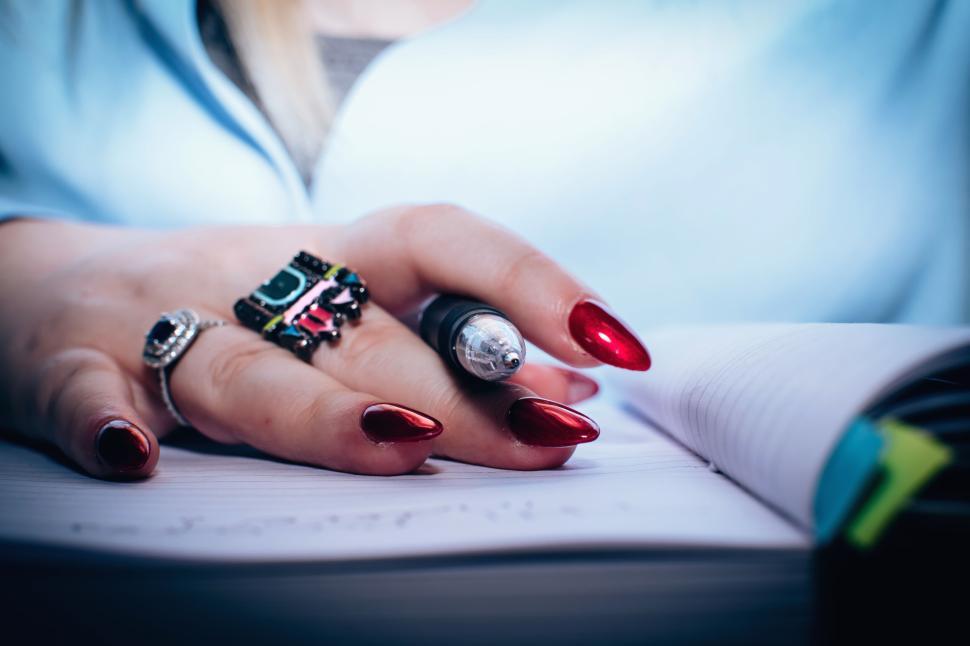 Free Image of Person taking notes with a stylish pen featuring unique red nails 