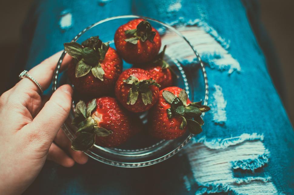 Free Image of Vibrant strawberries in a bowl placed over ripped denim, fresh and tasty 