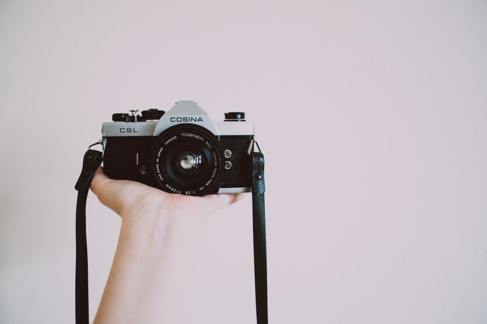 Free Image of Hand holding vintage Cosina camera against a plain white wall. 