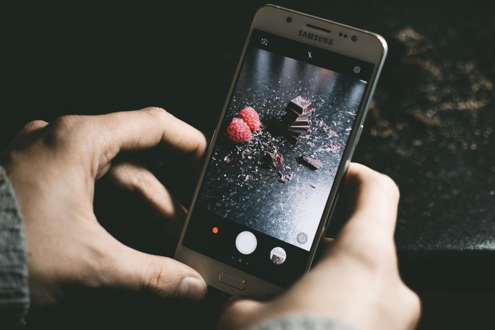 Free Image of Person holding Samsung phone photographing raspberries, chocolate. 