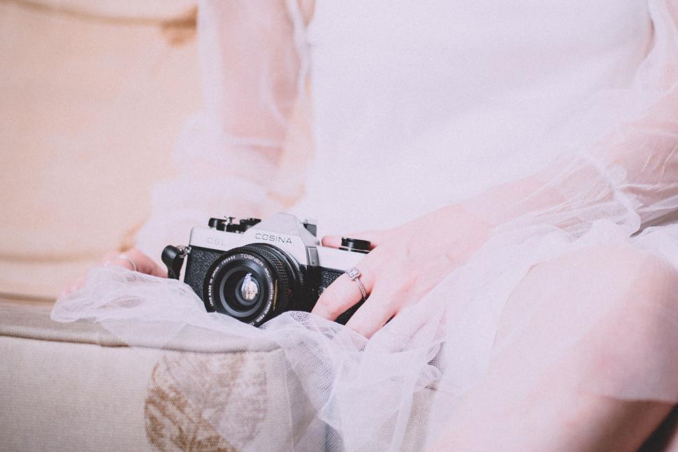 Free Image of Person holding vintage camera while in elegant white sheer dress. 