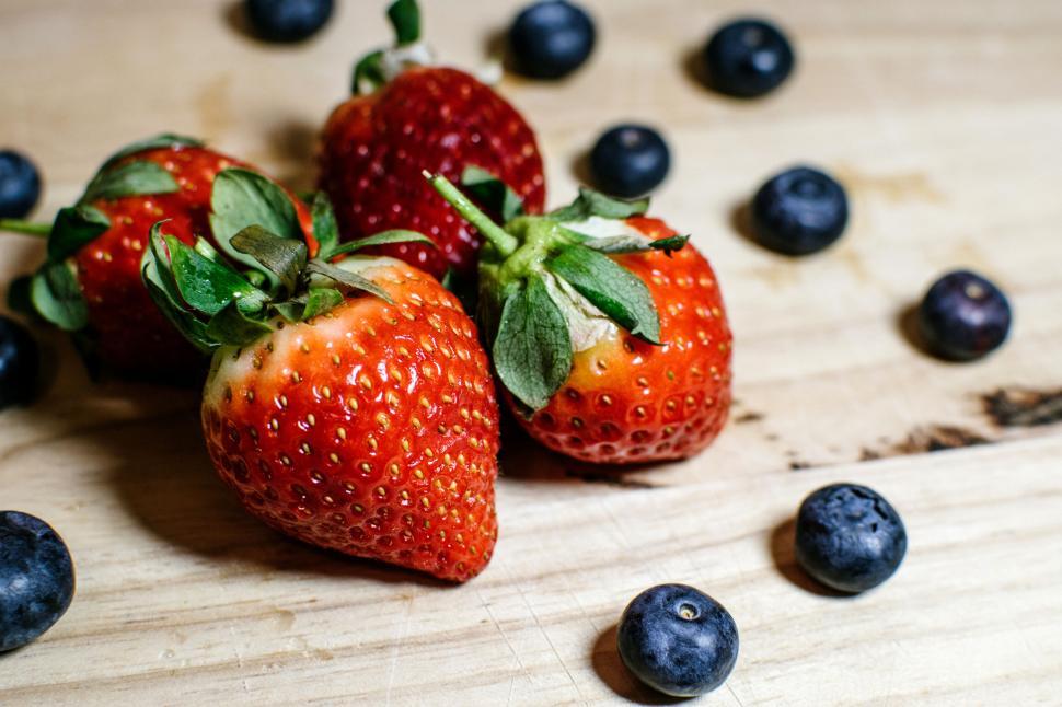 Free Image of Mix of strawberries and blueberries on a wooden surface background. 