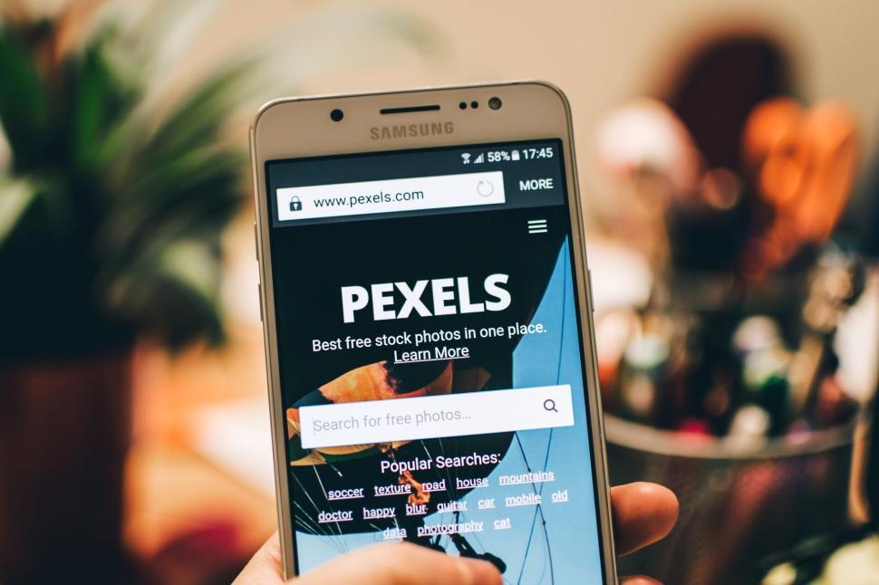 Free Image of Hand holding Samsung phone with Pexels website loaded on screen. 