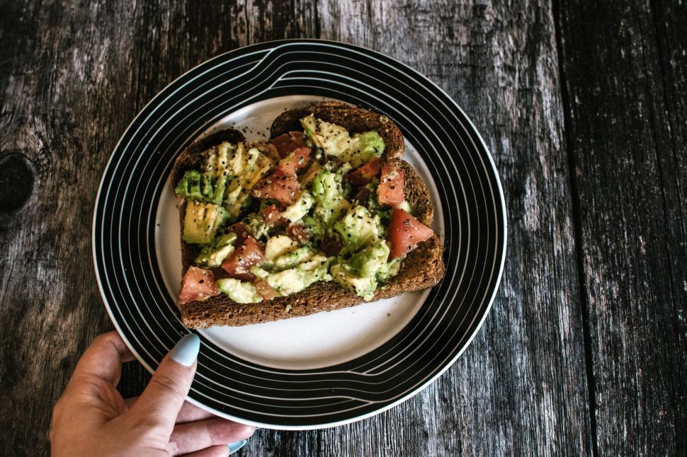 Free Image of Hand placing a toast with avocado and tomato on a striped plate. 