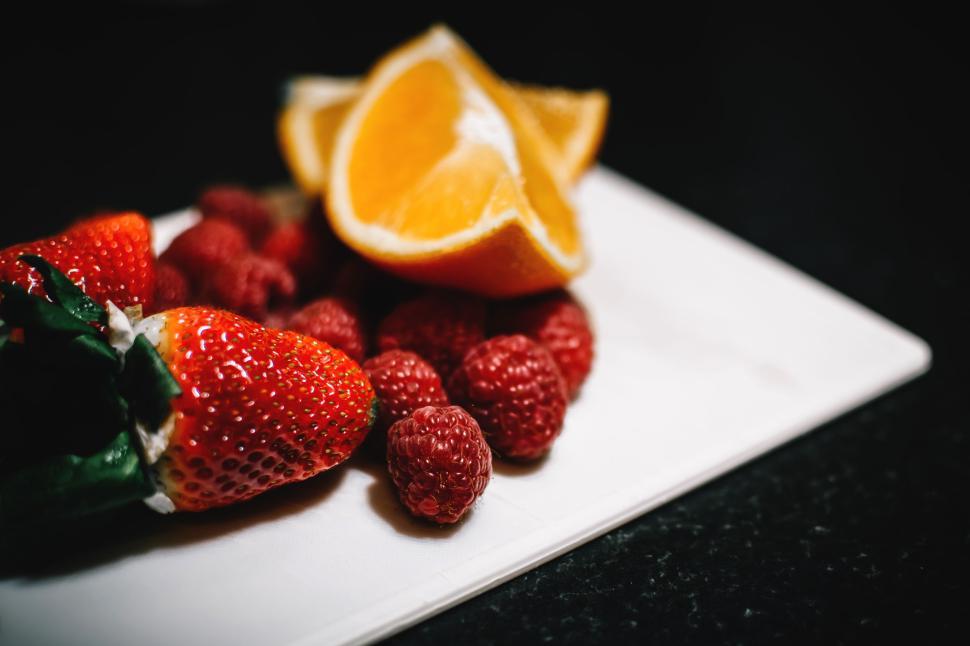 Free Image of Fresh strawberries, raspberries, and sliced oranges on a plate 