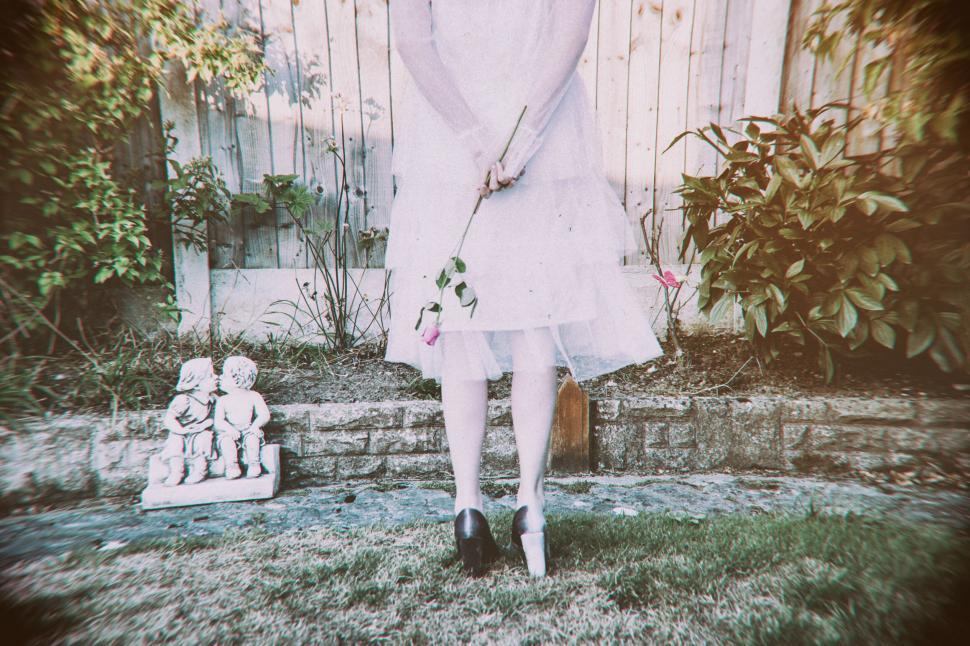 Free Image of Girl in a white dress holding a rose facing away in a garden 