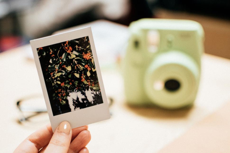 Free Image of Hand holding a photograph in front of a green instant camera 