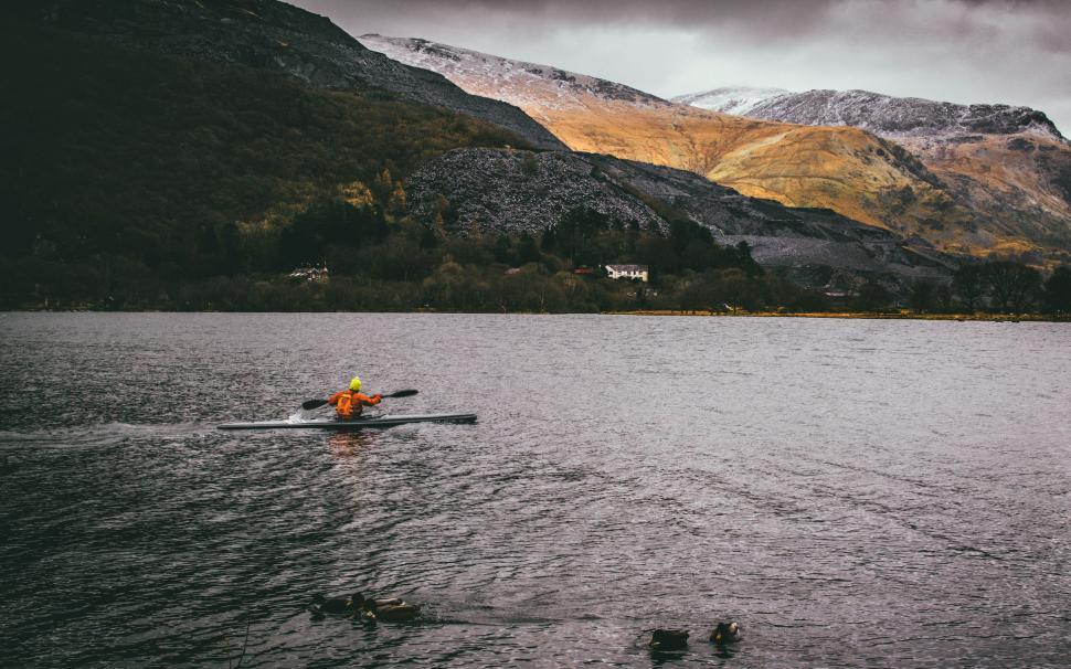Free Image of Person kayaking on a lake with a mountain background and cloudy sky. 
