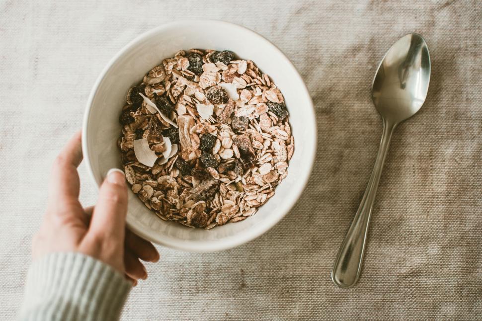 Free Image of Hand holding a white bowl filled with oats and a spoon on a beige background. 