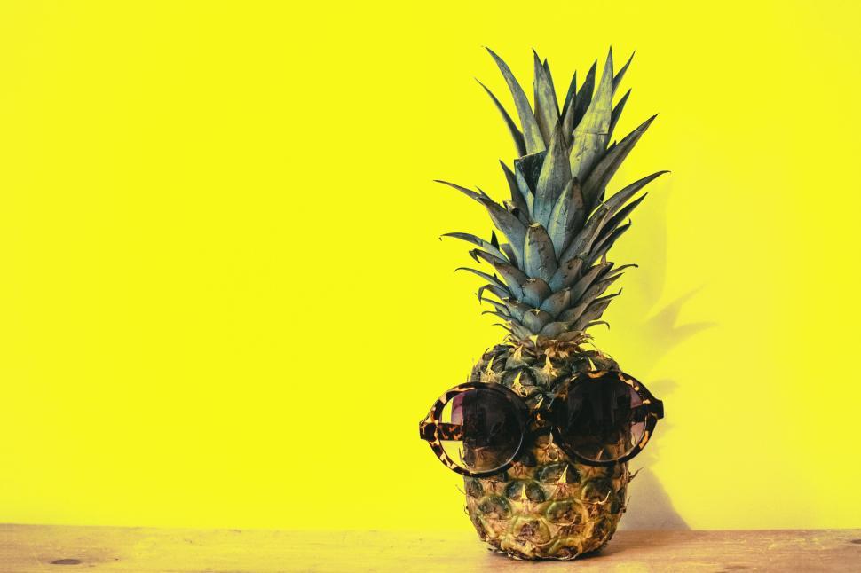 Free Image of Pineapple with sunglasses on a yellow background creating summer vibes. 