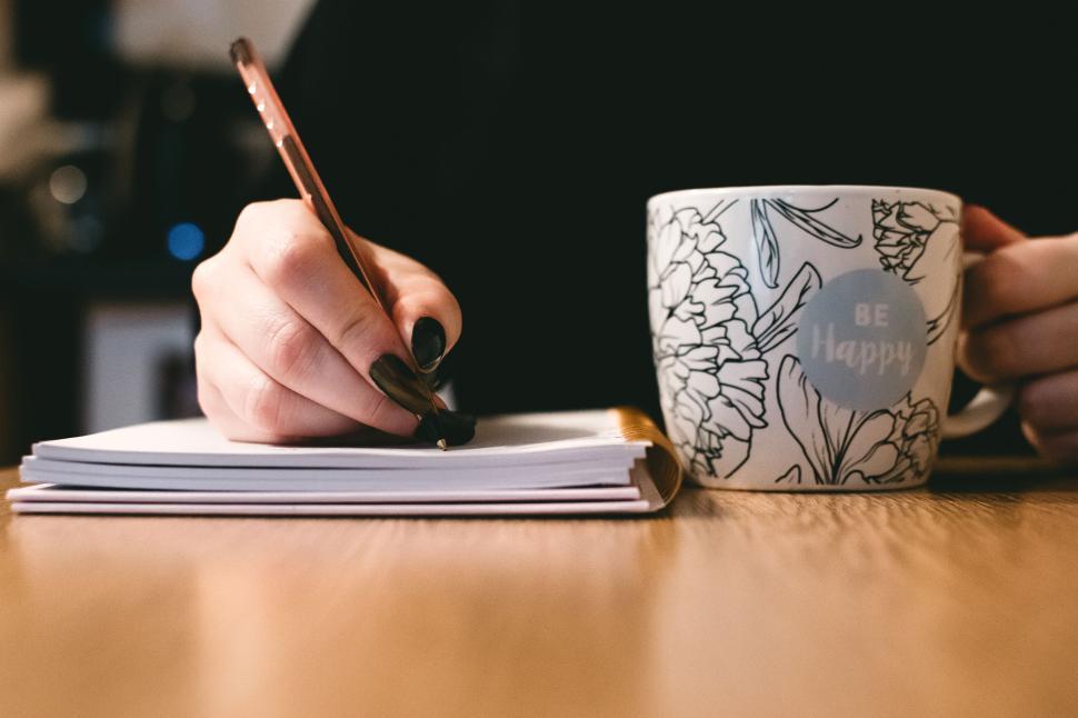Free Image of Person writing in notebook next to a coffee cup with motivational text. 