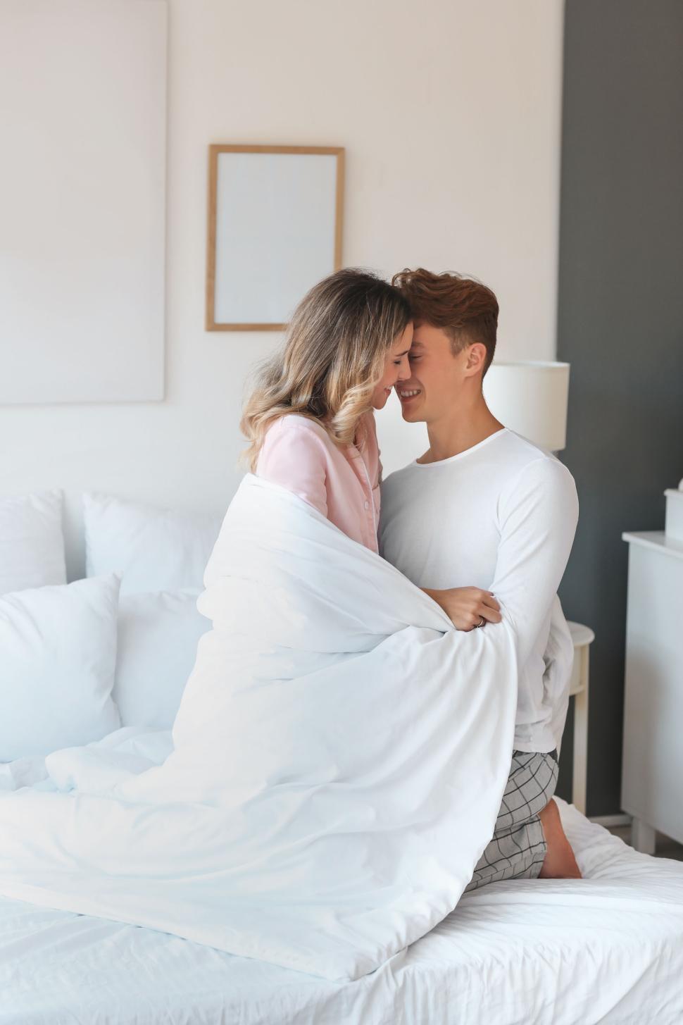 Free Image of Couple embracing on bed wrapped in blanket in cozy bedroom 