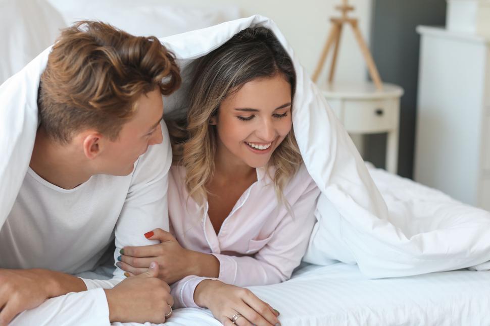 Free Image of Couple under blanket smiling on bed in cozy morning moment 