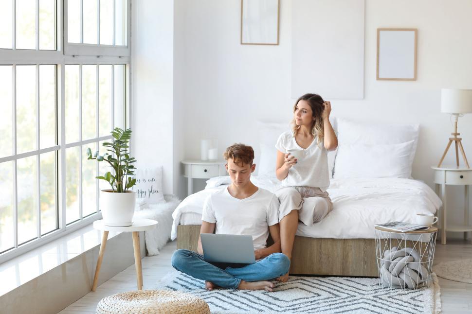Free Image of Woman on bed, man using laptop in bright, minimalist bedroom 