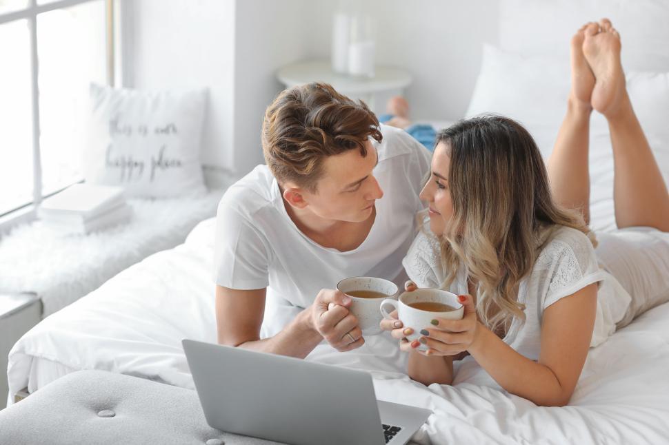 Free Image of Couple having coffee on bed looking at laptop in bright bedroom 