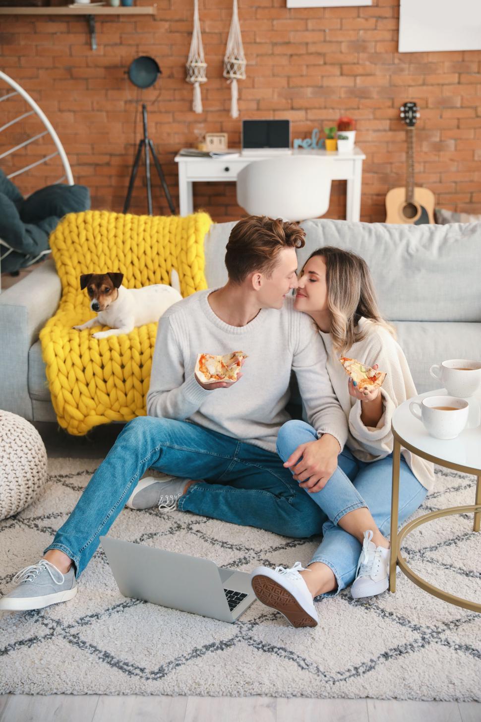 Free Image of Couple sharing pizza on floor while their dog sits nearby happily 