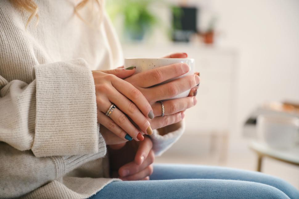 Free Image of Hands holding a coffee cup with a cozy sweater and warm setting. 