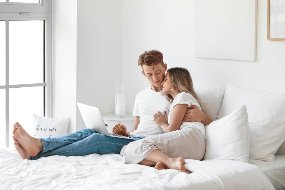 Free Image of Relaxed couple cuddling on bed with laptop in bright bedroom 