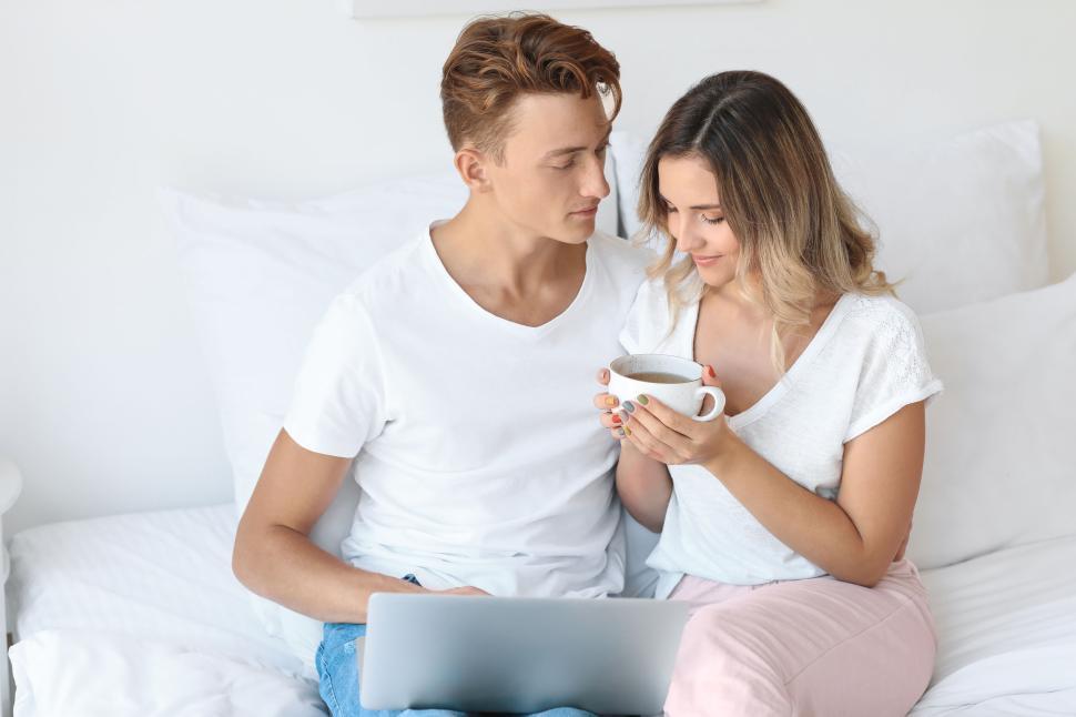 Free Image of Couple sitting on bed, woman holding coffee, sharing moment together. 
