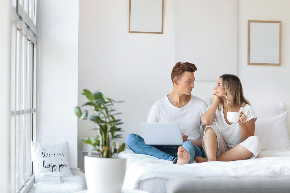 Free Image of Couple relaxing with a laptop and coffee on a cozy white bed. 