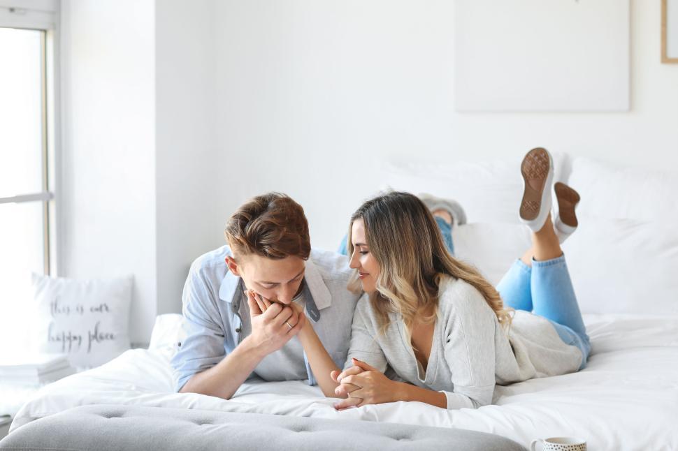 Free Image of Couple lying on a bed, holding hands in a cozy modern bedroom. 