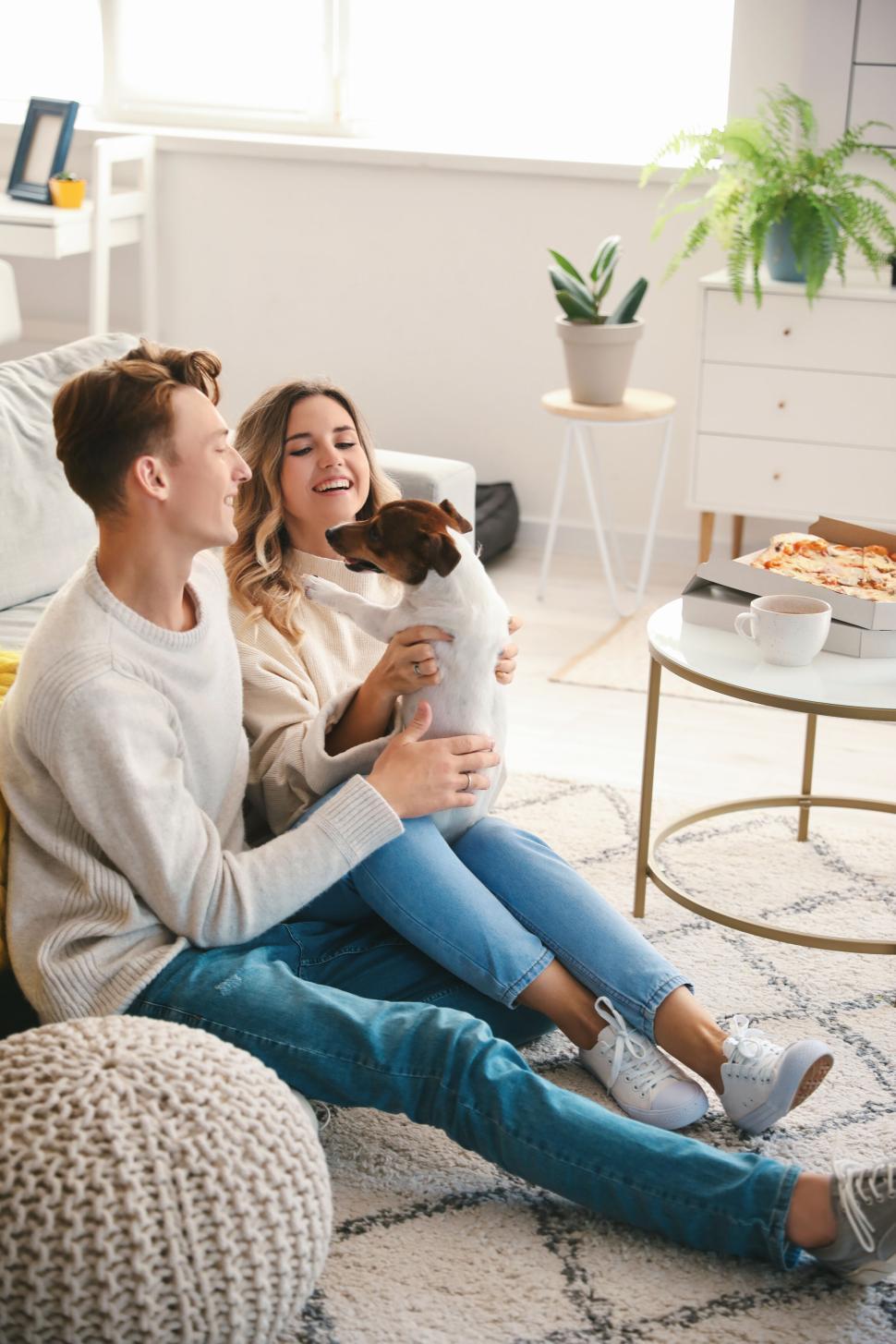 Free Image of Couple with dog on cozy couch, laughing and enjoying their time. 