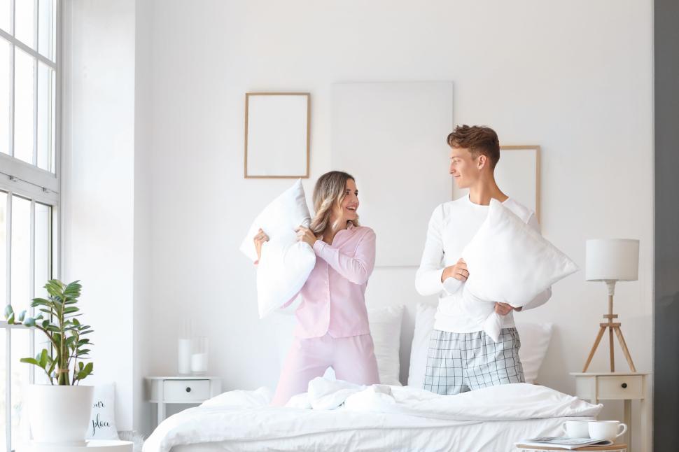 Free Image of Couple having playful pillow fight in bright modern bedroom. 