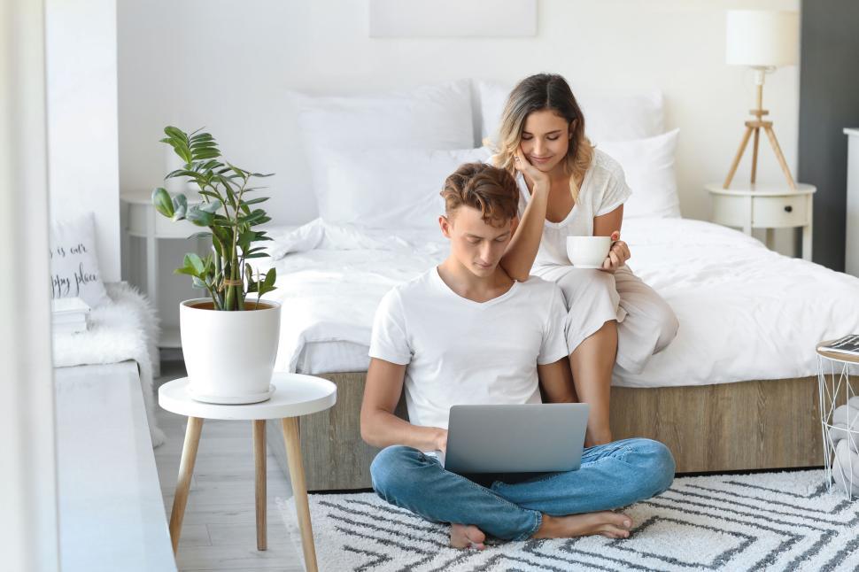 Free Image of Couple with laptop sitting on the floor by the bed, cozy morning 