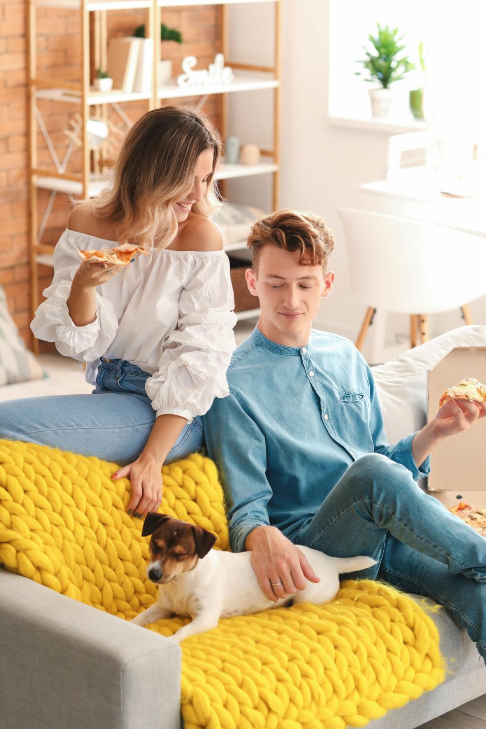 Free Image of Happy couple eating pizza on the couch with their cute dog 