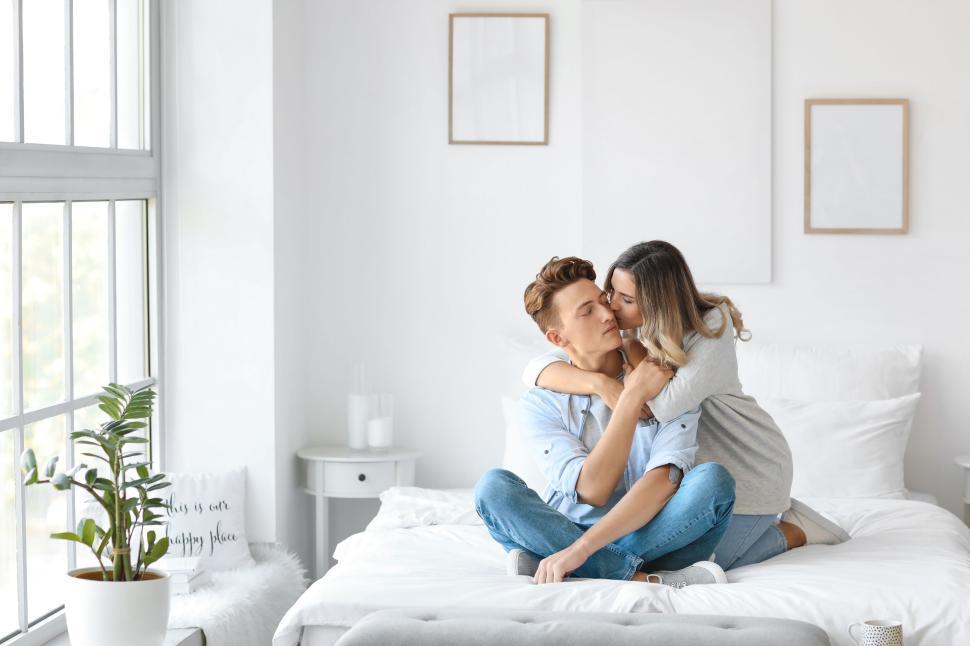 Free Image of Couple embracing on a bed in a white minimalist bedroom 