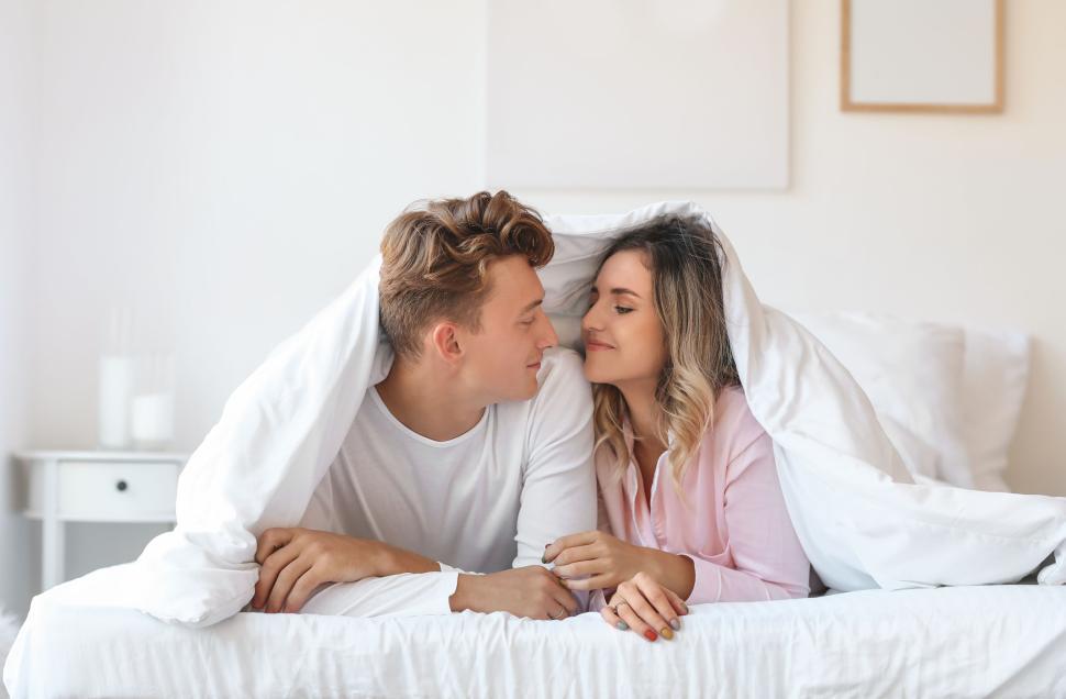 Free Image of A couple snuggling under the covers in a bright bedroom 